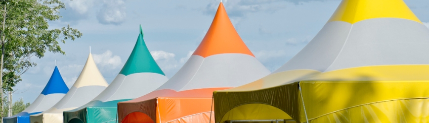 Five colorful carnival tents in yellow, orange, turquoise white and blue against a cloudy sky